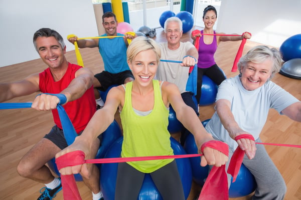 Portrait of happy men and women on fitness balls exercising with resistance bands in gym class